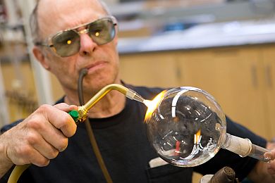 Roy Wentz uses a tube to blow air into an instrument he is repairing for the chemistry department. Wentz, 67, spent 10 years training his son the glassblowing trade, but many institutions have cut their in-house glassblowers, and the traditional knowledge is fading. (Photo: Martin Vloet, U-M Photo Services.)