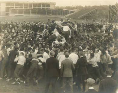crowd of male students shoving each other as some of them climb onto the heads and shoulders to fight.