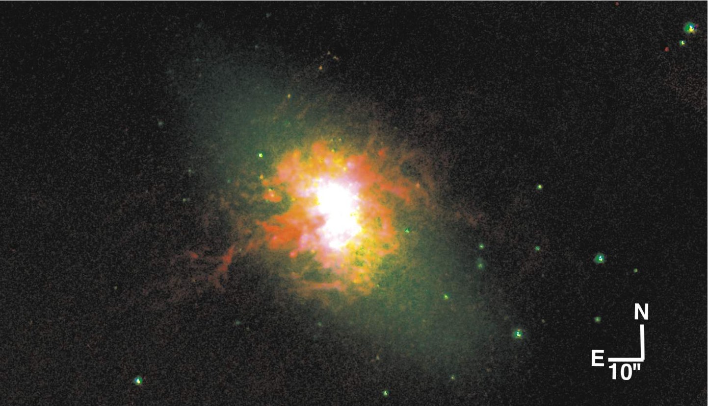 A three-color image of the dwarf starburst galaxy NGC 5253. Green corresponds to star light. The yellow shows the gas that is being lit up by the starburst at the galaxy's core. The red shows where ultraviolet light from massive stars is evaporating gas, exposing the central starburst along a narrow cone. Credit: Courtesy of Jordan Zastrow