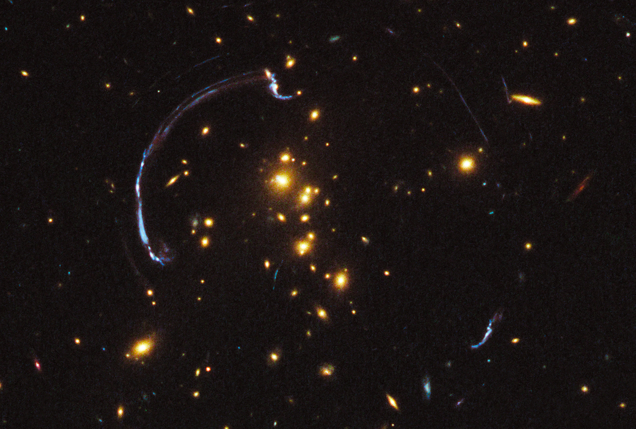 This new image from the Hubble Space Telescope shows a dramatic example of gravitational lensing. Gravitational lensing occurs when light from a distant source passes through space that is warped by a massive foreground object. The warped space acts as a natural zoom lens, magnifying and distorting the image of background object. The background object is a galaxy that appears as a nearly 90-degree arc of light in the foreground galaxy cluster RCS2 032727-132623. Image credit: NASA, ESA, J. Rigby, K. Sharon, M. Gladders and E. Wuyts