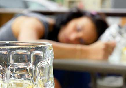 Alcohol abuse: drunk young woman or student lying down on a table with beer bock still in hand, focus on glass up front. (stock image)