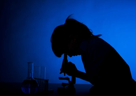 Sillouette of a woman peering into a microscope. (stock image)