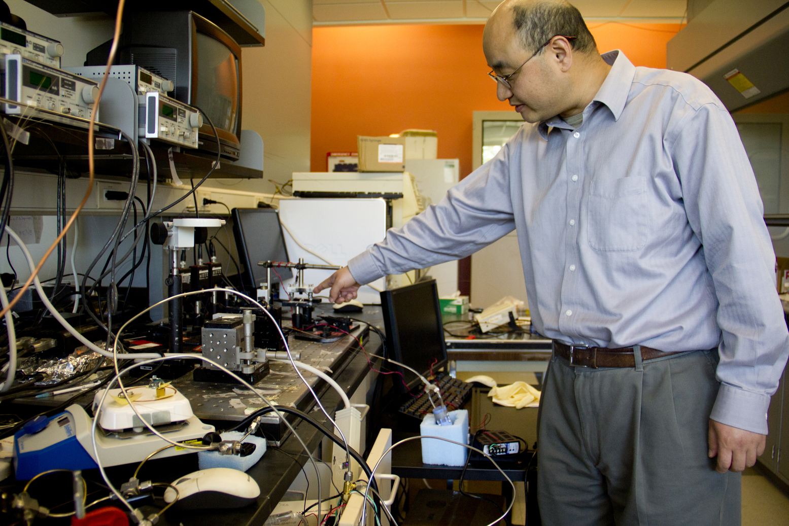 Xudong Fan, an associate professor of biomedical engineering, points to the compressor that is part of the smart, portable gas sensor that he is developing. The device could one day be used to detect chemical weapon vapors or indicators of disease more precisely than current models do. It also consumes less power, which is crucial for stretching battery life in a mineshaft or an isolated clinic. Image credit: Joseph Xu, College of Engineering