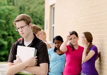 A group of teens make fun of another student outside of a school. (stock image)