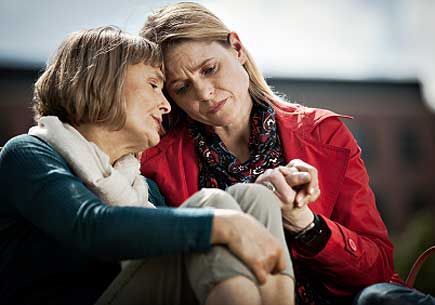 Mature women sitting close to each other with sad expression on their faces. (stock image)