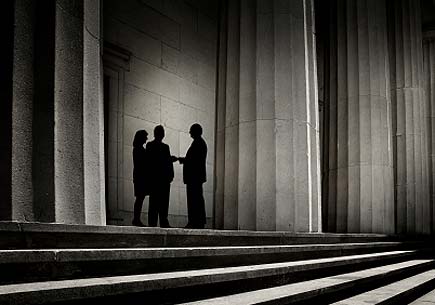 Three people, silhouetted against a backdrop of power, shaking hands. (stock image)