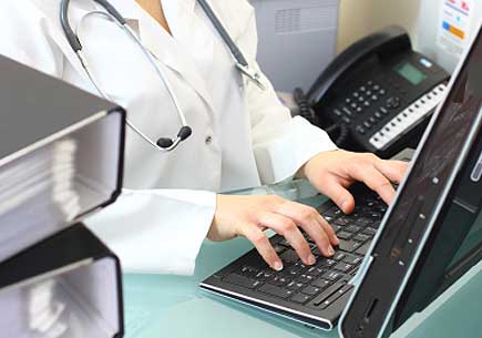 Cropped photo of a person wearing a lab coat and stethoscope typing on computer keyboard. (stock image)