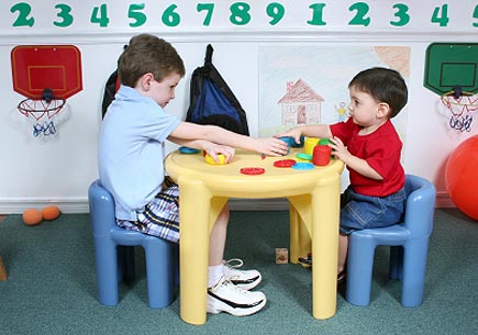 Four year old and two year old boy playing with colorful dough at preschool. (stock image)