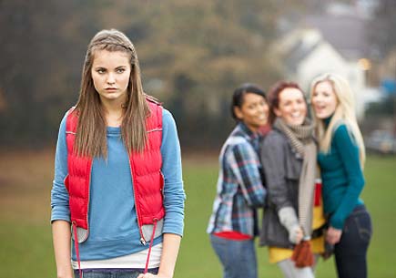 Upset teenage girl with friends gossiping in background behind her back. (stock image)