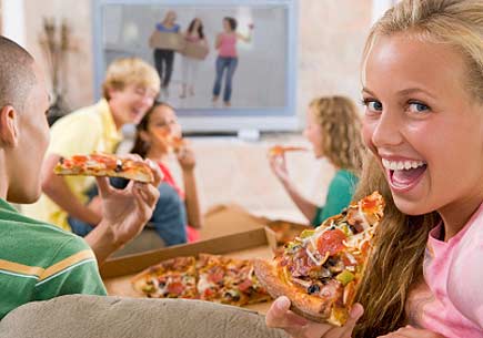 Teenagers hanging out in front of the television eating pizza. (stock image)
