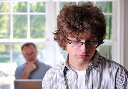 Somber teenage boy with his father in the background. (stock image)