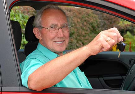 A senior man sits in a car smiling and holding up a set of keys. (stock image)