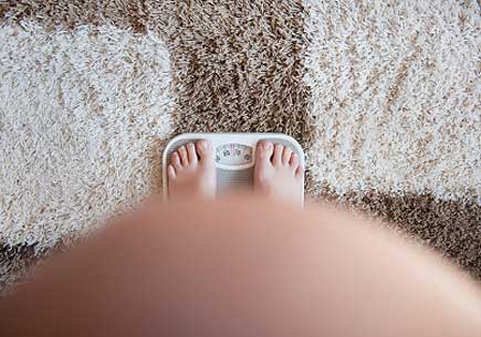 Pregnant woman weighting herself on a bathroom scale. (stock image)