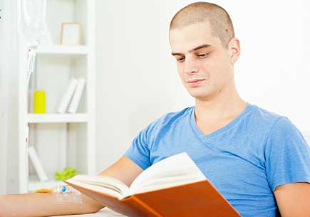 Young man having chemotherapy treatment at home and reading a book. (stock image)