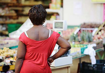 Rear view of an African American woman surveying a market's produce section. (stock image)