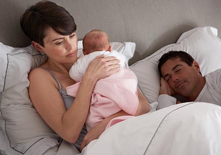 Mother cuddling newborn baby in bed while husband sleeps. (stock image)