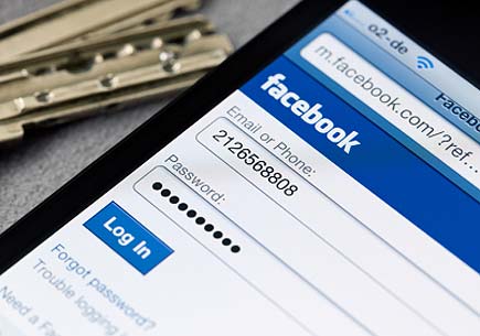 Facebook login page on iPhone display, keys in background. (stock image)