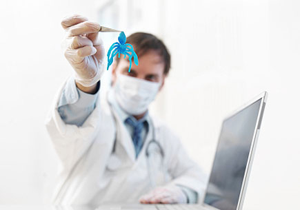 A masked doctor holds up a blue "virus" in front of a laptop computer. (stock image)