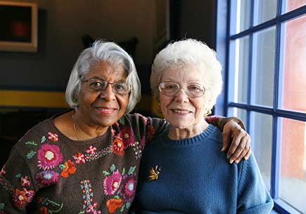 Two senior women embrace in front of a window. (stock image)