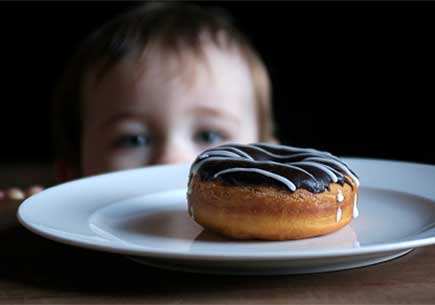 A child looks longingly at a donut just out of reach on the table. (stock image)