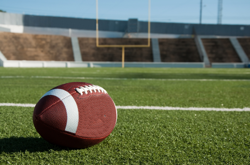 A football on a stadium field with goal posts in the background. (stock image)