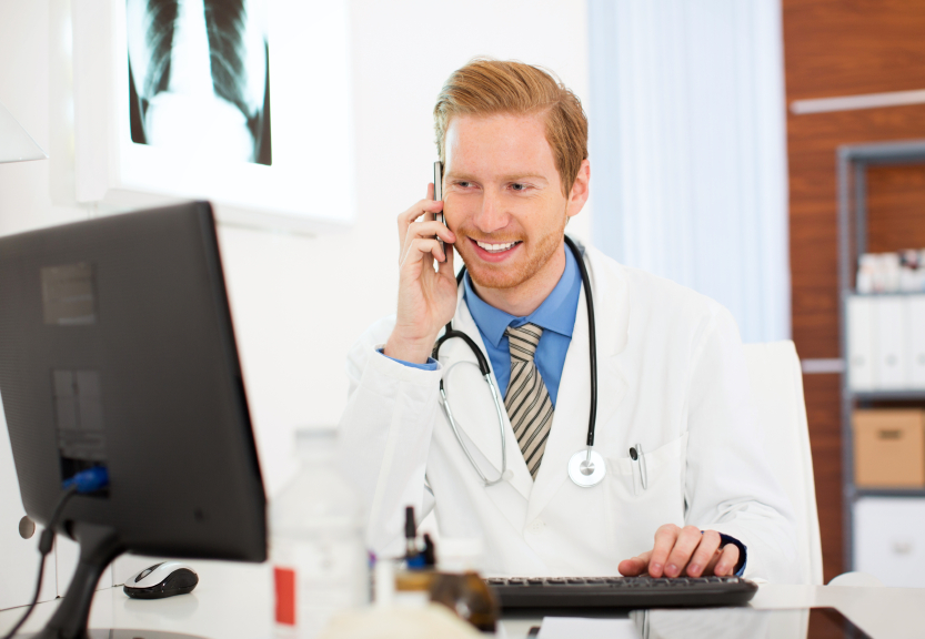 A doctor on the phone and looking at a computer screen. (stock image)