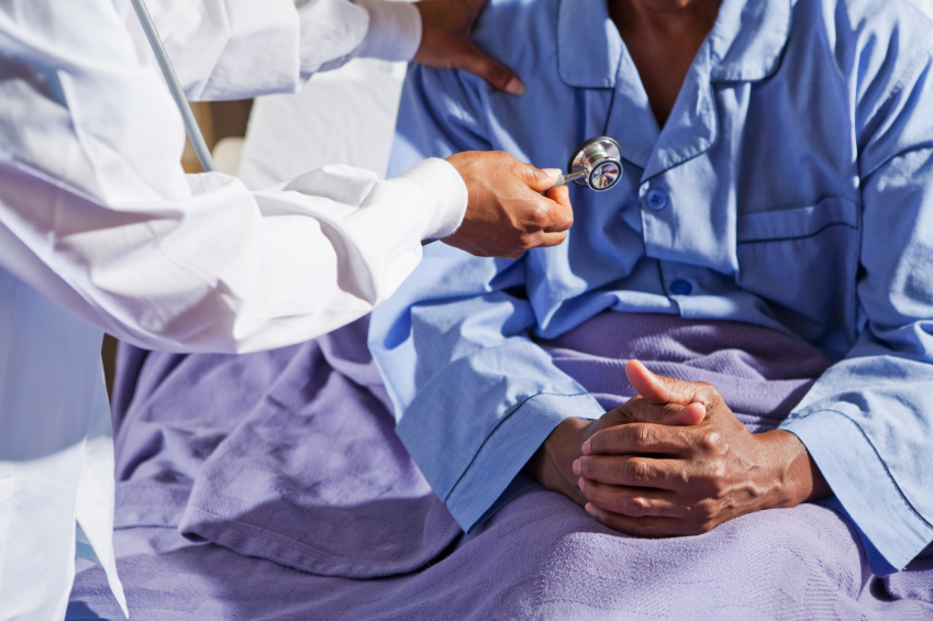 Doctor holding stethoscope with patient in hospital bed. (stock image)