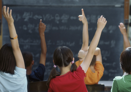 A group of children raising their hands in class. (stock image)
