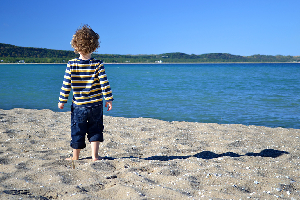 A young child stands on a beach looking out at one of the Great Lakes. Image credit: Michigan Sea Grant