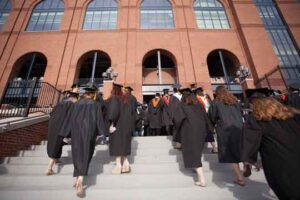 Students approach Michigan Stadium for commencement. Dressed in black robes, pictured from behind walking up stairs.