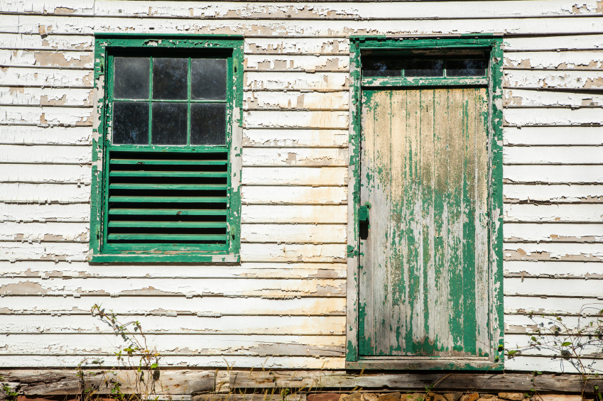 Exterior of a house with peeling paint and an old window and door. (stock image)