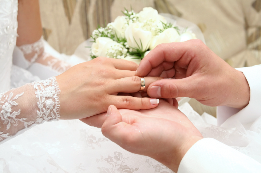 Tightly cropped image of a groom placing a wedding band on his bride's finger. (stock image)