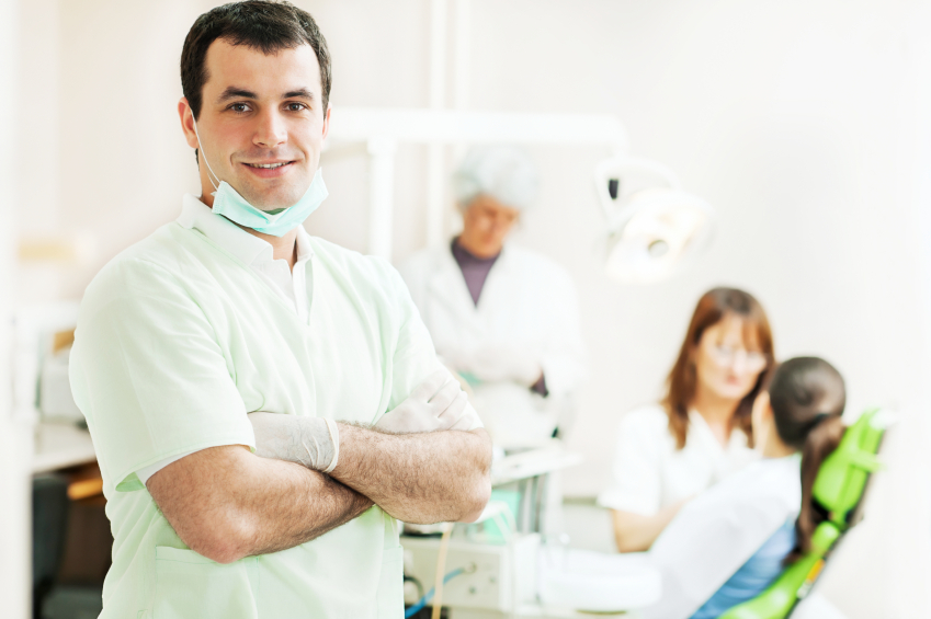 A dentist looks at the camera in the foreground while two assistants work with a patient. (stock image)