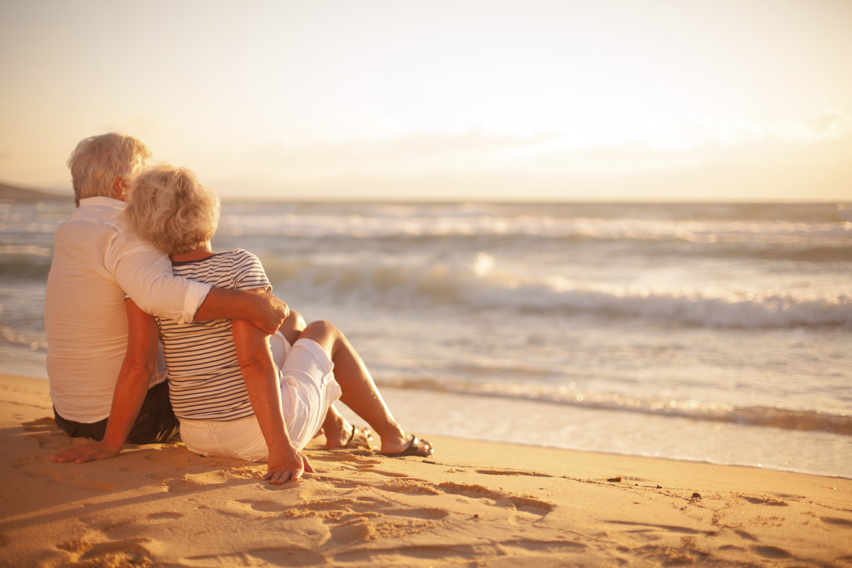 Older couple sitting on a beach during sunset. (stock image)