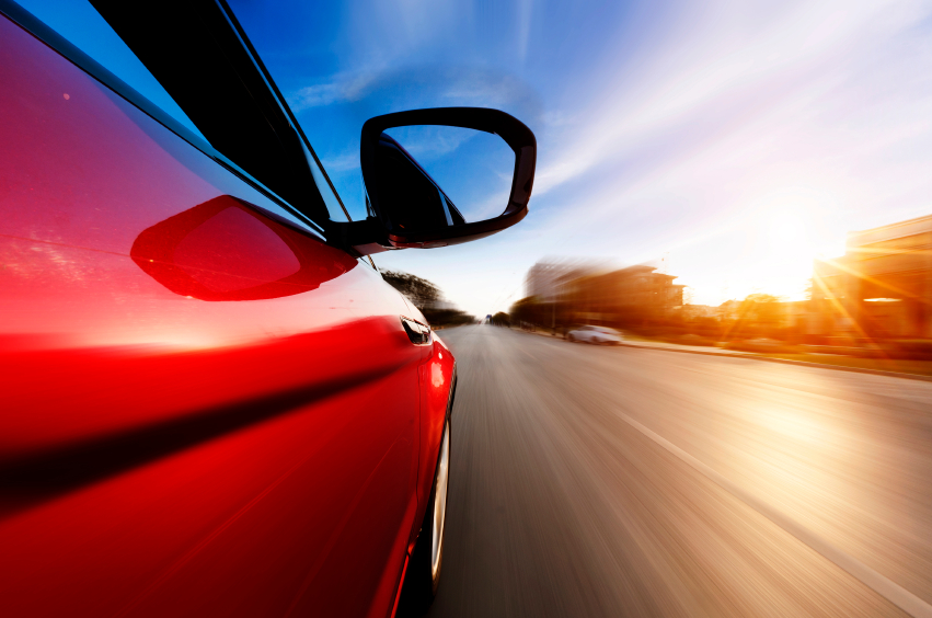 Red car speeds along a road. (stock image)