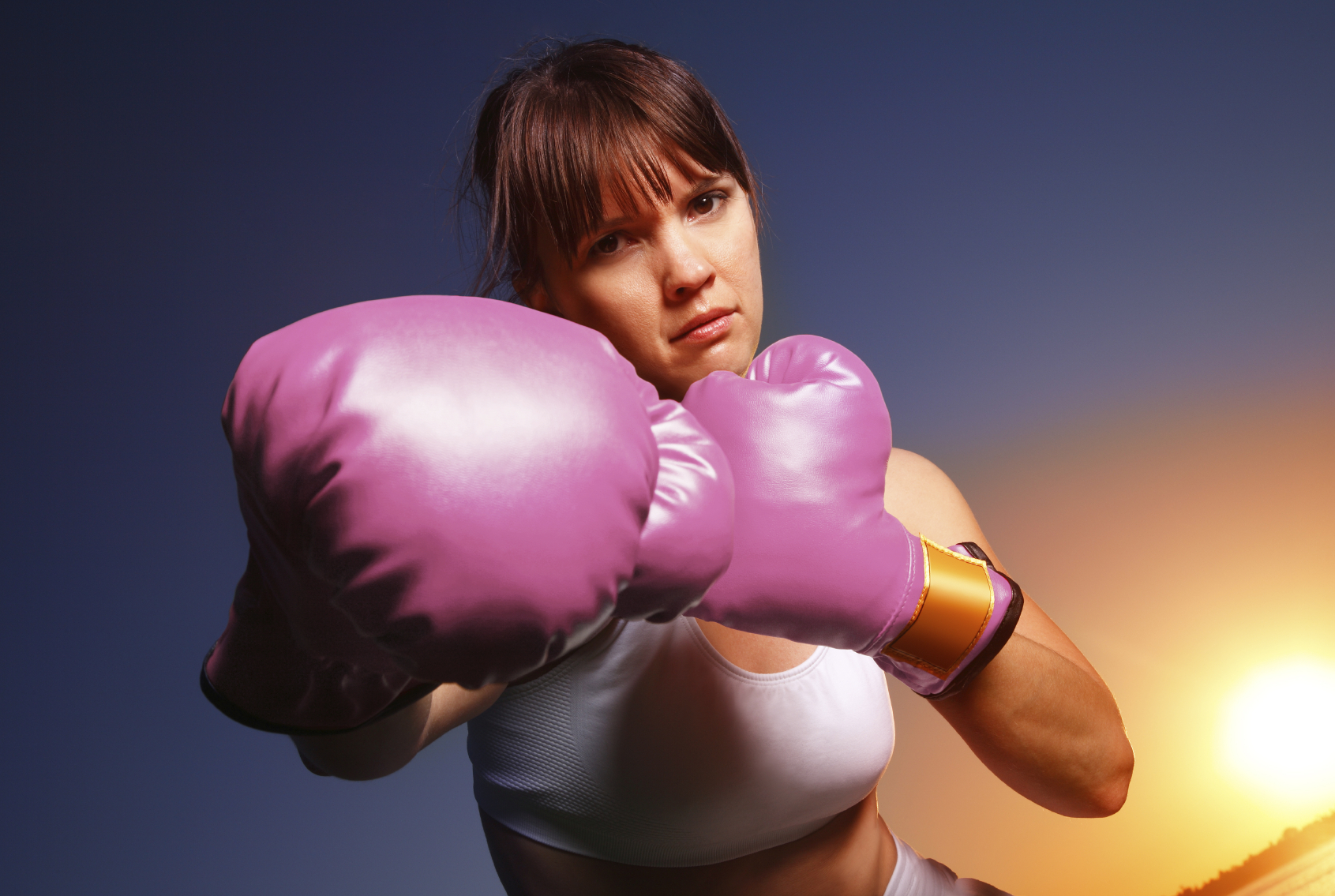 A woman wearing pink boxing gloves metaphically fights cancer. (stock image)