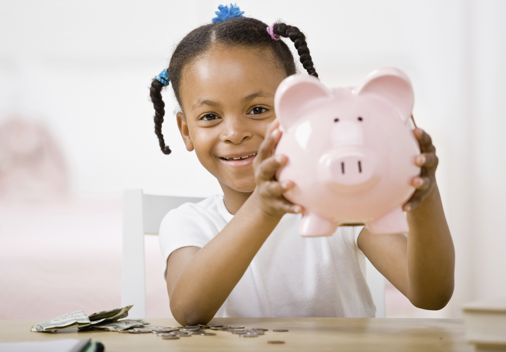 A young girl proudly holds up her piggy bank. (stock image)
