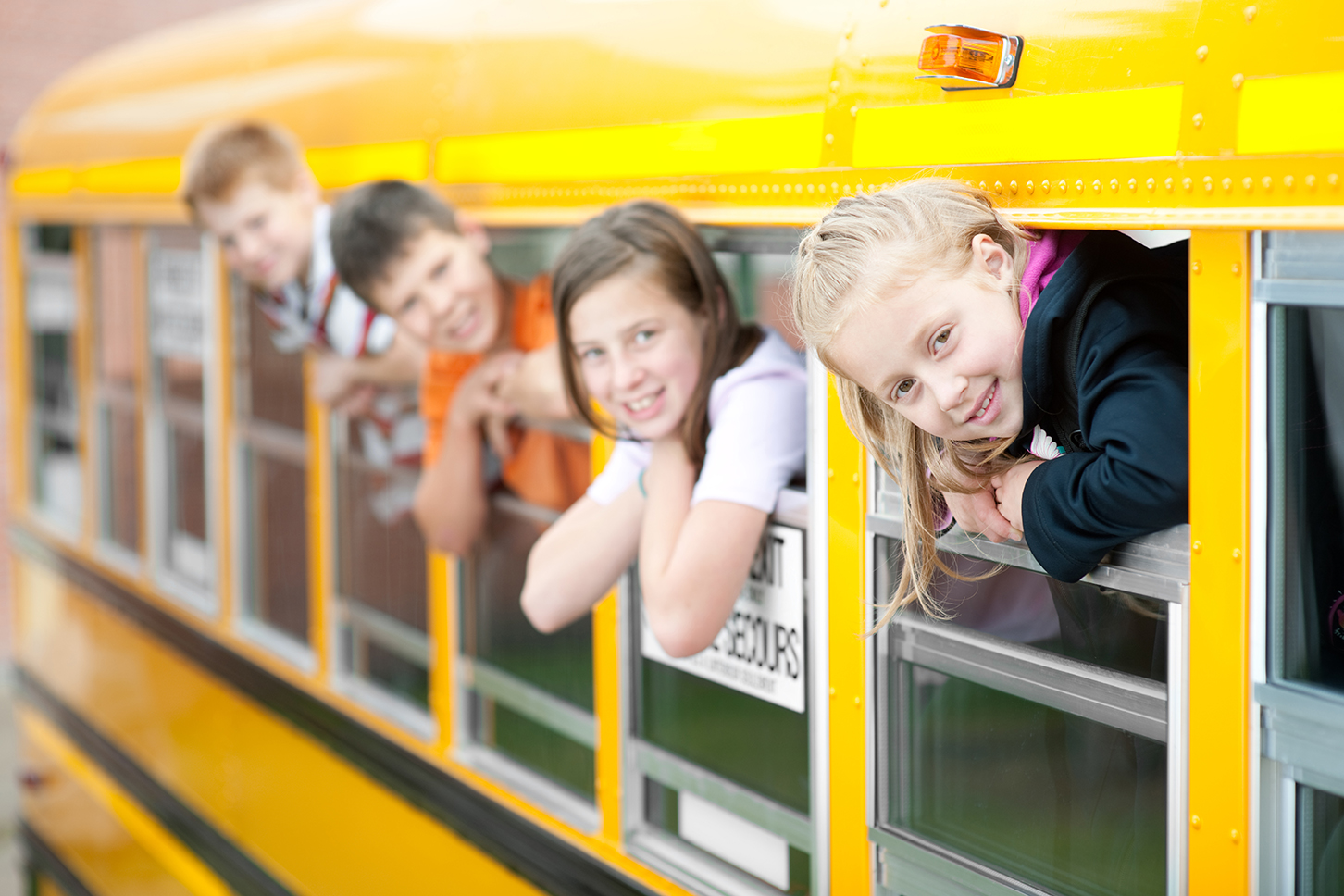 School children lean out of school bus windows. (stock image)
