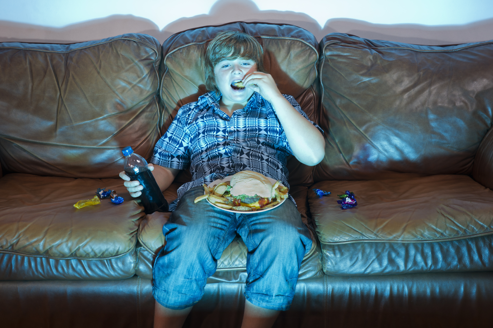A young boy eats junk food in the glow of the television. (stock image)