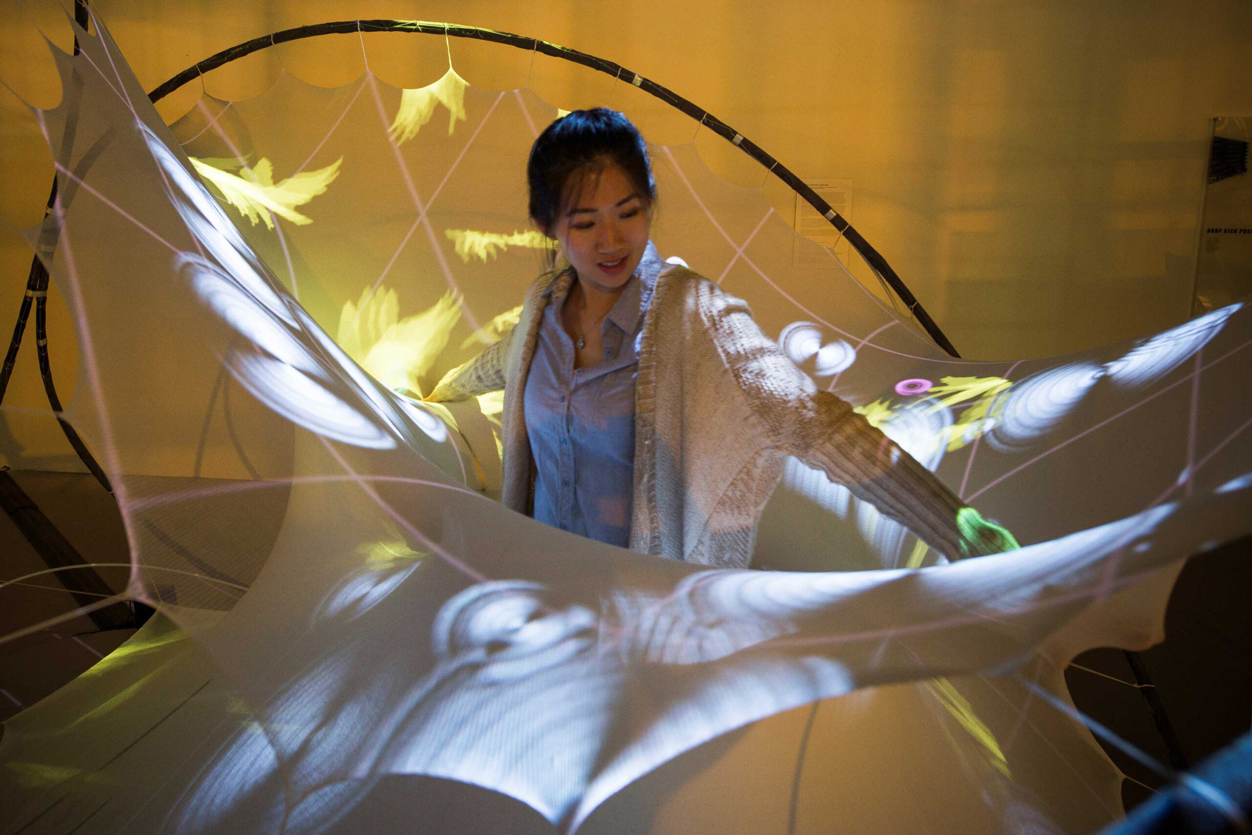 Architecture student Karen Duan interacts with a 3-D structure titled StretchPLAY, one of the pieces designed to encourage responses from autistic children. Pressing on the elastic textile in particular spots activates animations that are projected across various areas of the textile surface. Image credit: Sean Ahlquist
