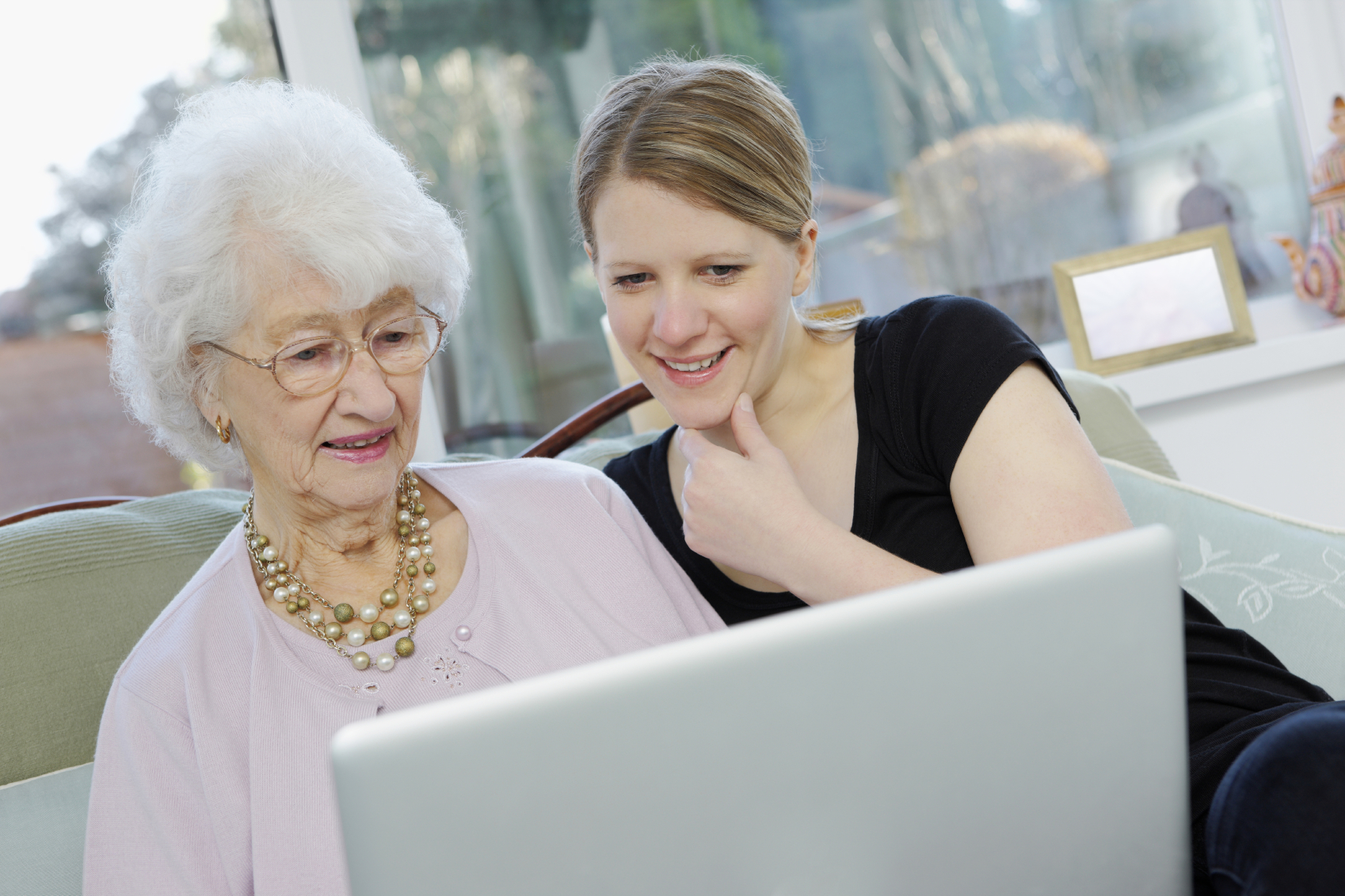 Young woman with her grandmother working on laptop at home. (stock image)