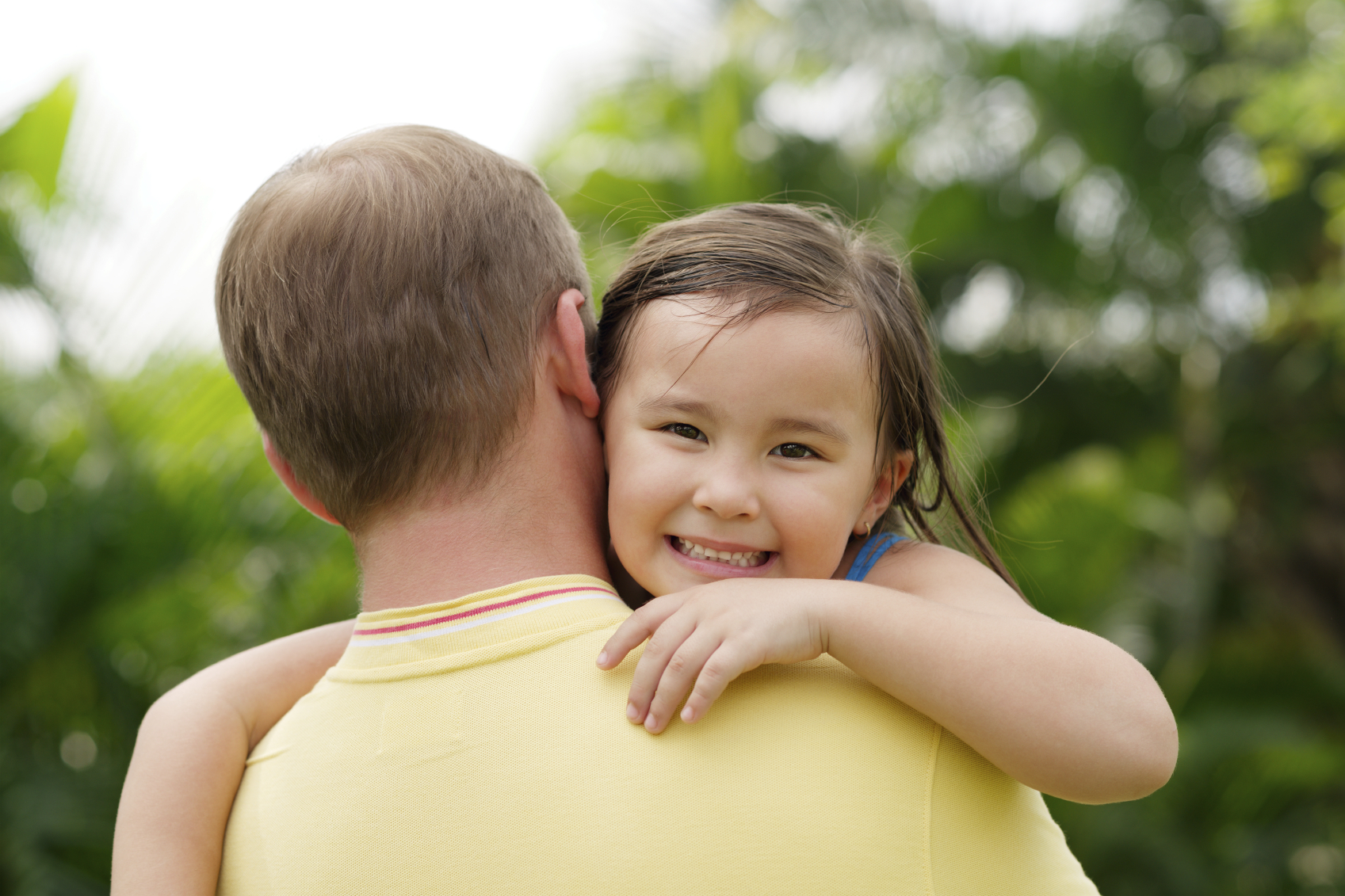 A little girl looks over her dad's shoulder while he hugs her. (istock image)