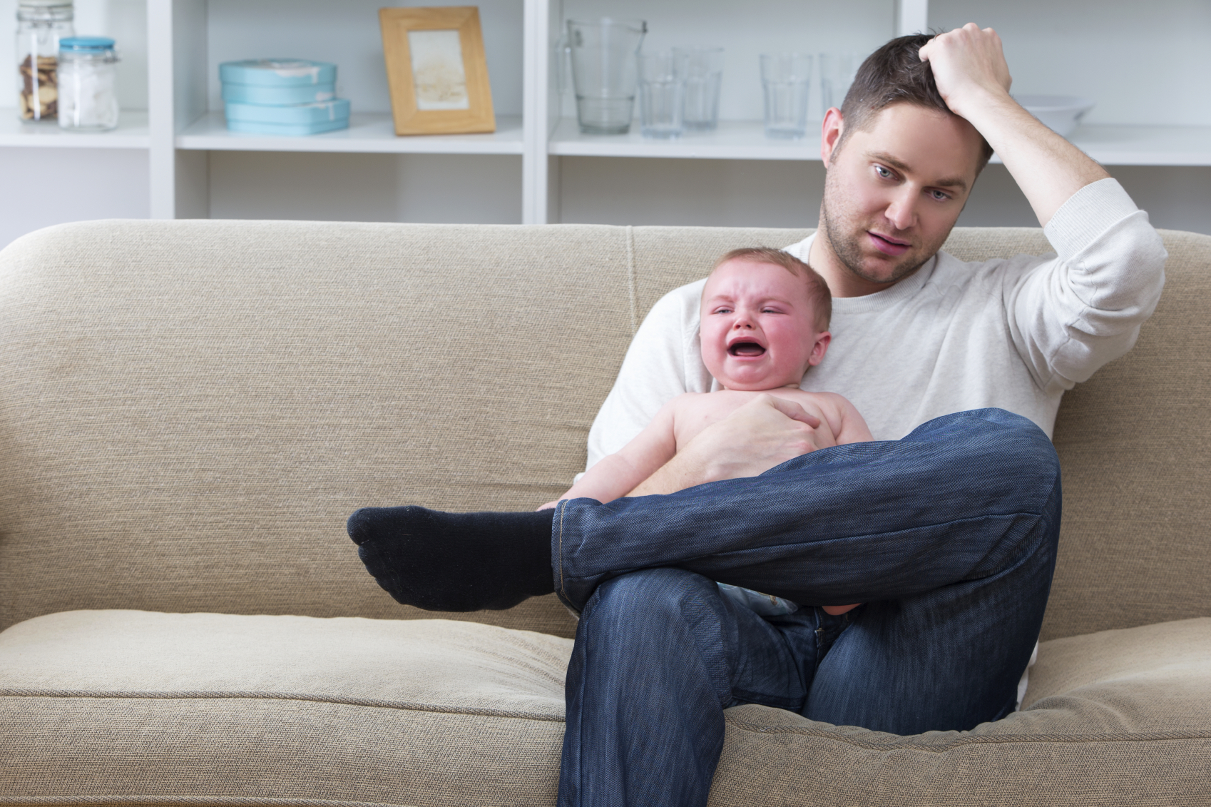 A man sitting on the couch with a crying baby. (stock image)