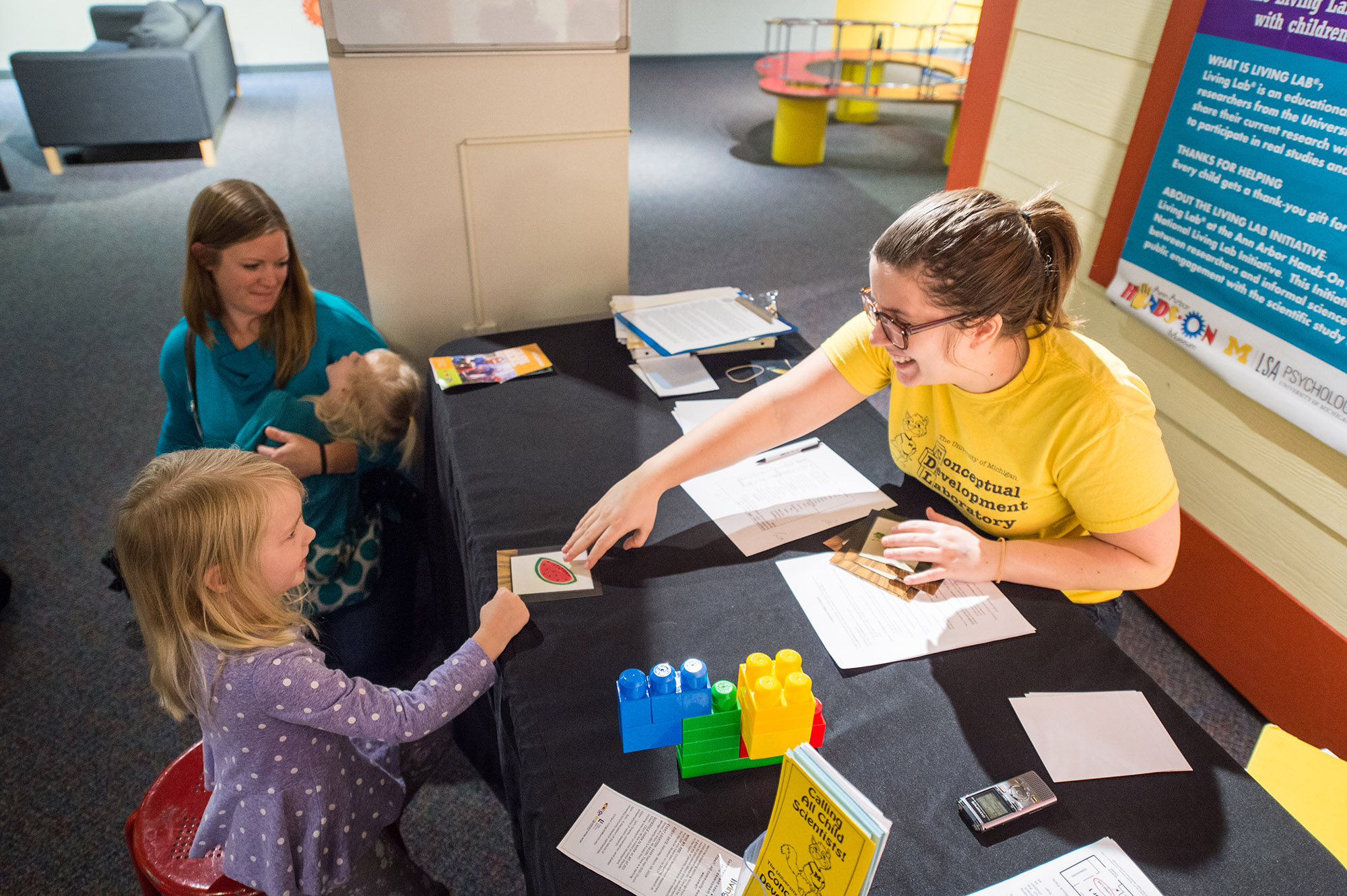 Merranda McLaughlin, lab manager shows cards to Natalee Hill as her mother Elizabeth looks on. Natalee is taking part in The Living Lab Program, a partnership between U-M, the Ann Arbor Hands-On Museum, the Natural History Museum and the Ann Arbor District Library. Natalee’s answers lend insight into how young children think about abstract concepts and categories. Image credit: Austin Thomason, Michigan Photography