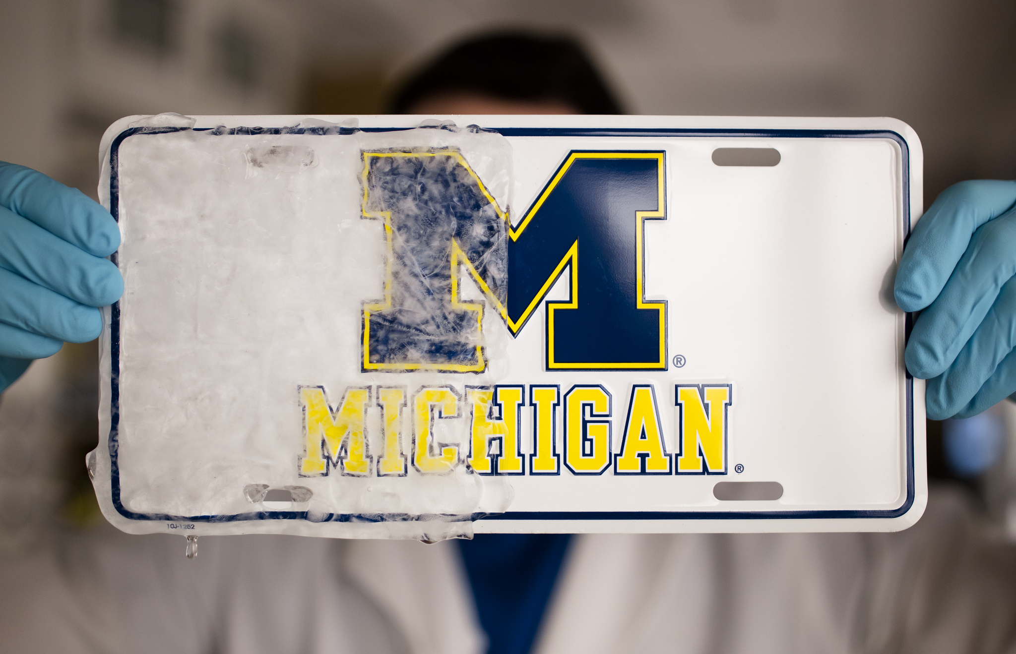   Kevin Golovin, a graduate student in materials science and engineering at U-M, demonstrates a new rubbery material that can create ice repelling, or "icephobic," coatings on a variety of materials, such as windshields or ship hulls. In this photo, the "icephobic" coating was applied to the right half of a license plate, preventing ice from sticking to that half after being placed in a freezer. The research is being done under the direction of Anish Tuteja, an associate professor in U-M's Department of Materials Science & Engineering. Image credit: Evan Dougherty, Michigan Engineering