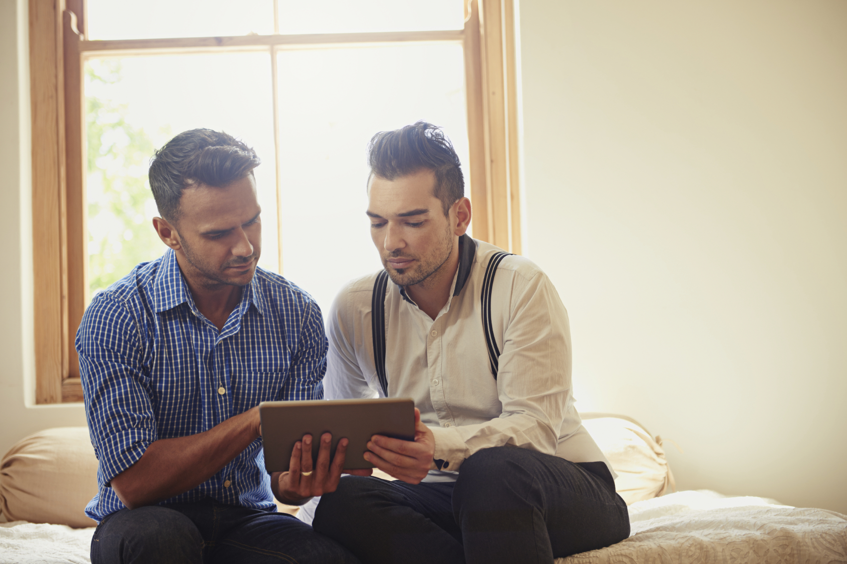 A gay couple looks at a tablet. (stock image)