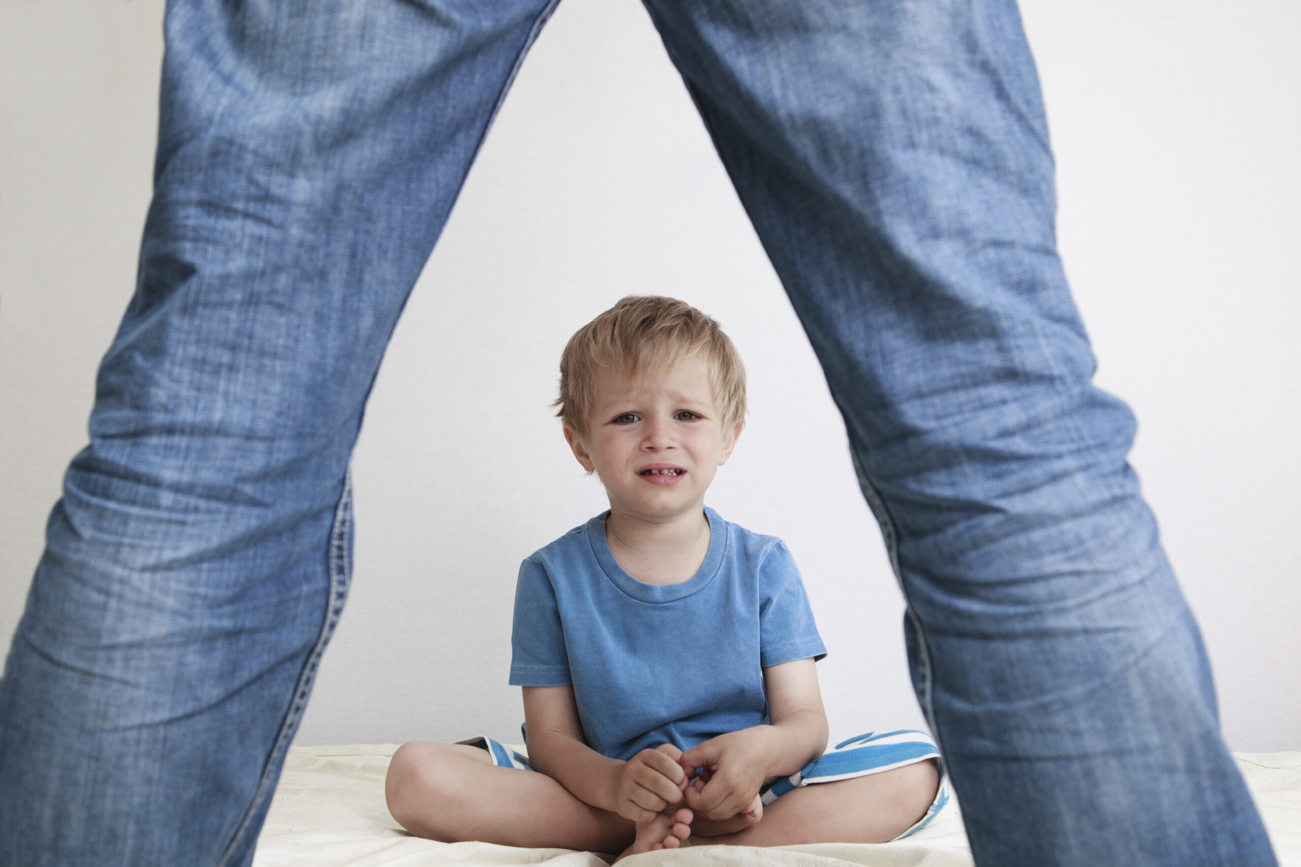 A parent stands looking down at a child on the floor. (stock image)