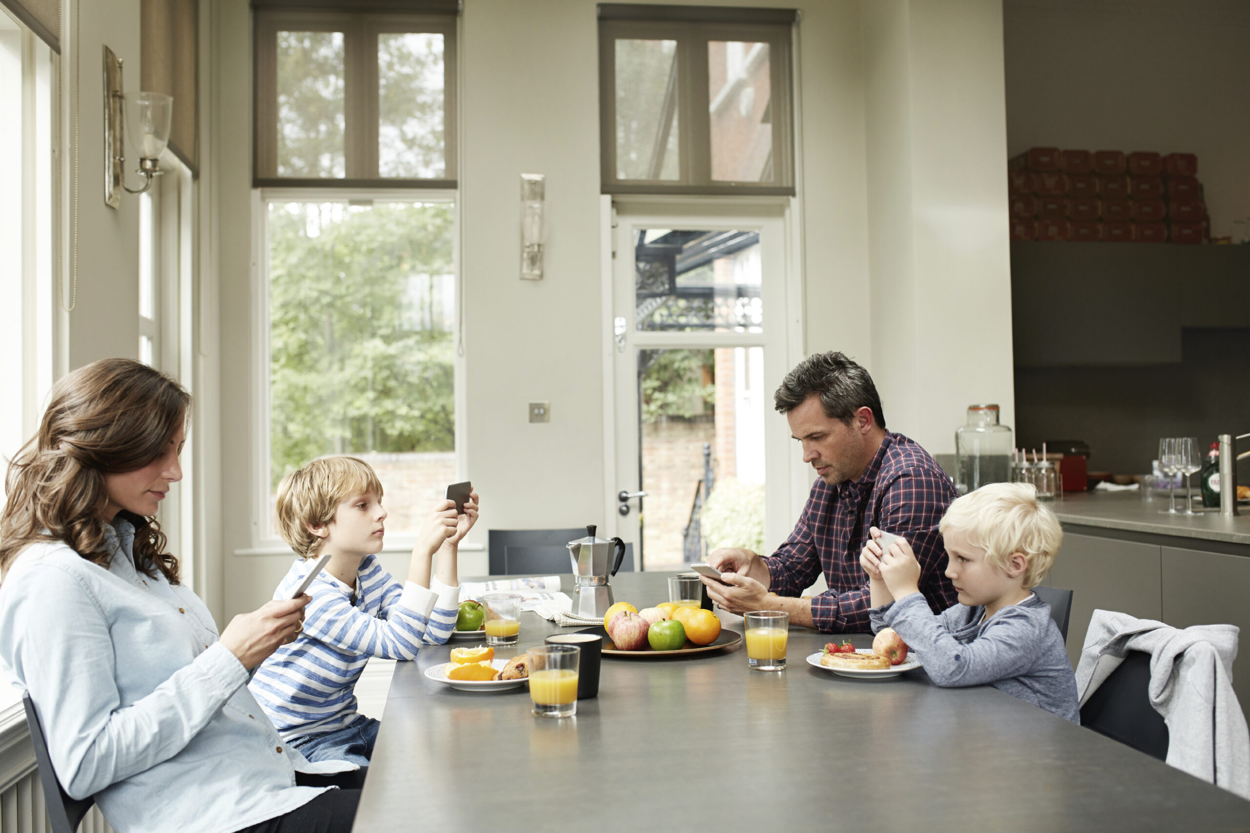 A family of four using cell phones at breakfast table. (stock image)