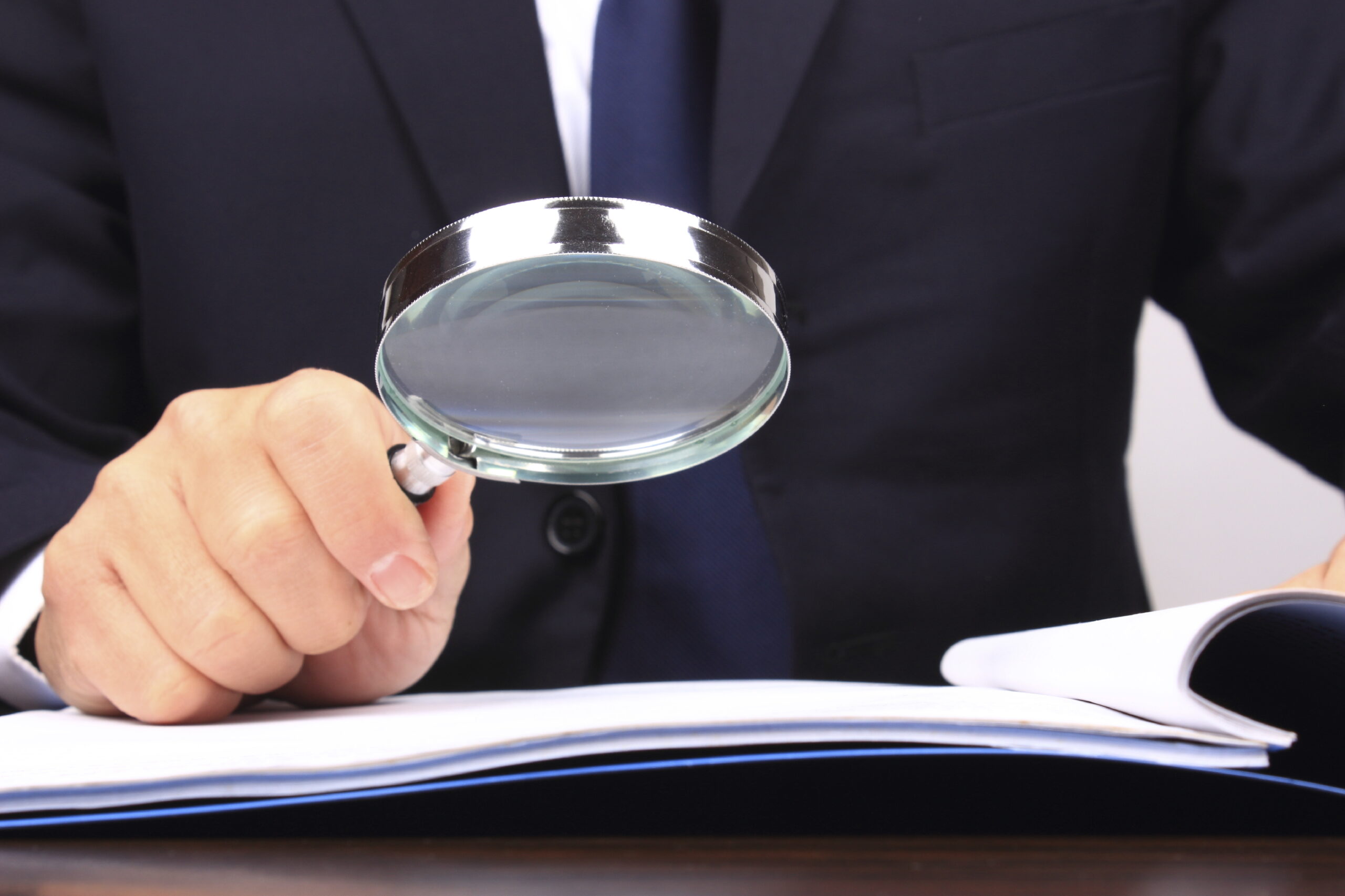 A man examines a report with a magnifying glass. (stock image)