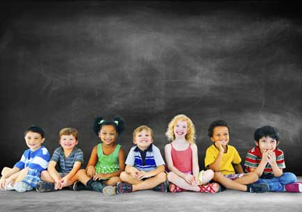Several children sit in front of a chalkboard. (stock image)
